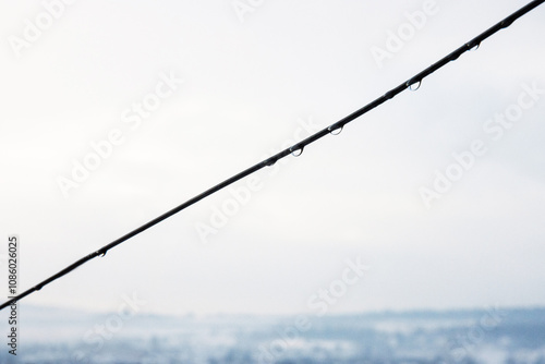 Minimalistic closeup of vineyard wire with delicate water droplets against cloudy overcast sky. Rain drops against a blurred horizon. Copy space
 photo