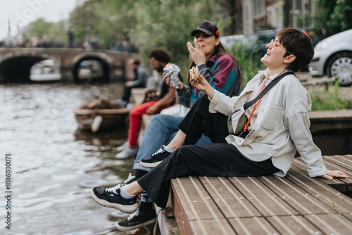 Canvas Print Lesbian couple enjoying a relaxed afternoon by a canal in Amsterdam, laughing and eating together, showcasing love and happiness during travel