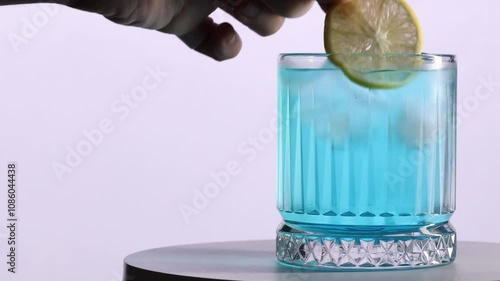 Lemon added to blue cocktail on white background