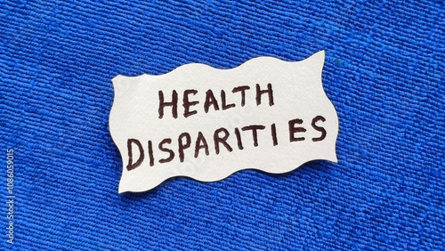 Health disparities word letters text handwritten calligraphy design on white paper label note isolated on a blue background surface with copy space. Closeup macro top view. Health disparities concept.