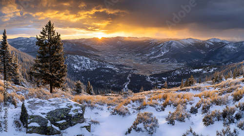 A breathtaking view of a snowy mountain valley at sunset, featuring dramatic clouds and golden light.