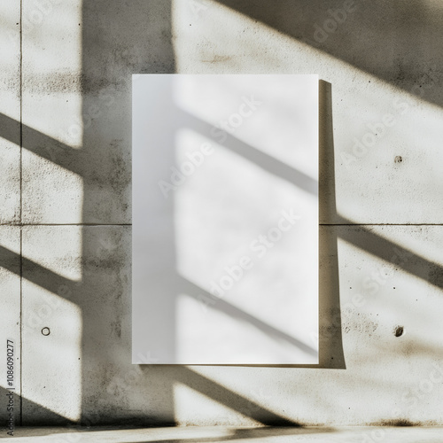 Frontal view of a white, unprinted sheet of paper hanging on a light gray concrete wall in a sunlit room photo