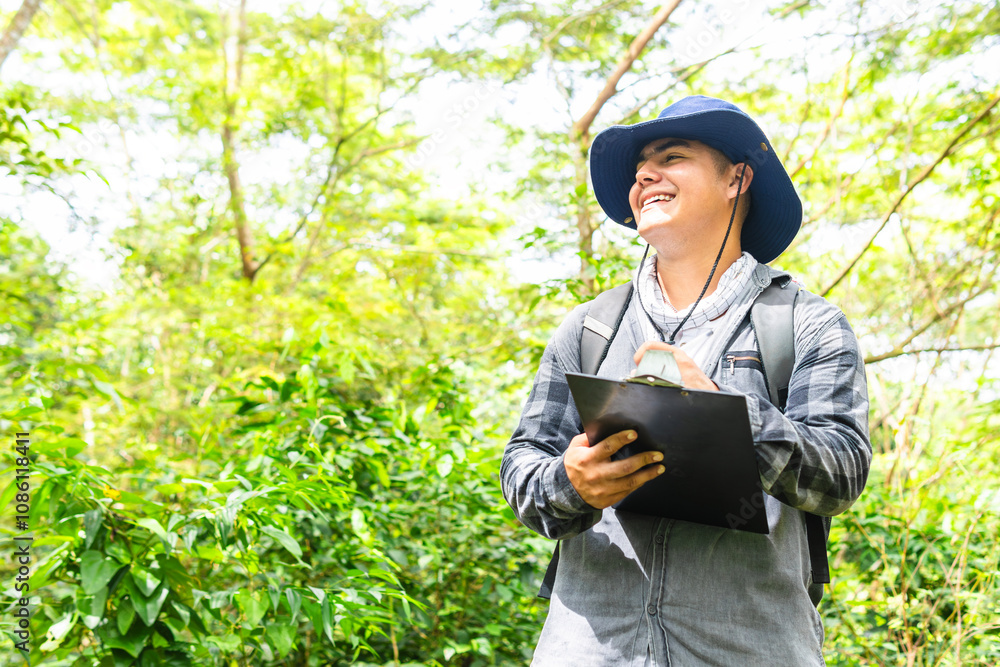 A young Colombian biologist, wearing a hat, smiles at the horizon with trees in the background while holding a notebook in the Amazon rainforest A young Colombian biologist, wearing a hat, smiles at the horizon with trees in the background while holding a notebook in the Amazon rainforest