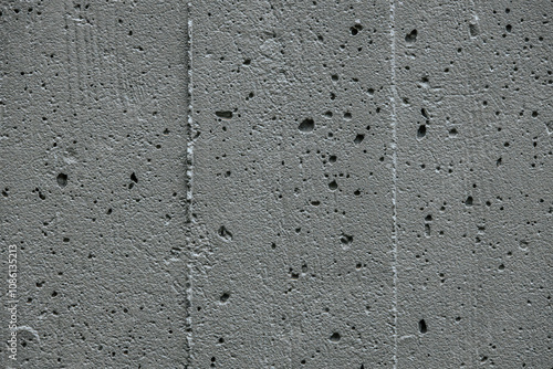 A detailed close-up of a rough, porous concrete surface. The texture features small holes and cracks, showcasing the raw and industrial appearance of the material.