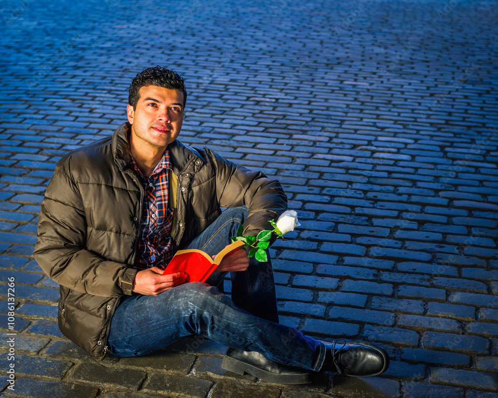 A man in a casual jacket sits on a cobblestone path, holding a white rose and an open book. He gazes thoughtfully into the distance, illuminated by soft, cool lighting..