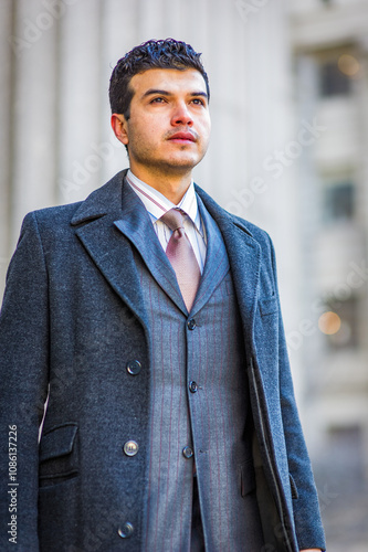 Obraz na płótnie A man in a stylish gray coat and suit stands confidently outdoors, looking into the distance. The background features blurred architectural elements that suggest an urban setting.. w salonie