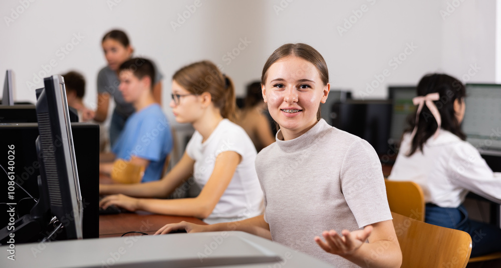Cheerful teenage caucasian girl sitting at desk in computer class, explaining, gesturing and looking at camera. Cheerful teenage caucasian girl sitting at desk in computer class, explaining, gesturing and looking at camera.