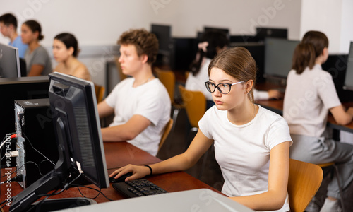 Focused female student in glasses using PC and studying computer science in the classroom