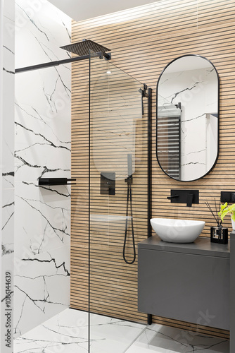 Modern interior of bathroom with ceramic wash basin with black faucet , wooden brown striped tiles on the wall and mirror. Luxurious hygiene room in industrial style with shower and glass. Vertical.