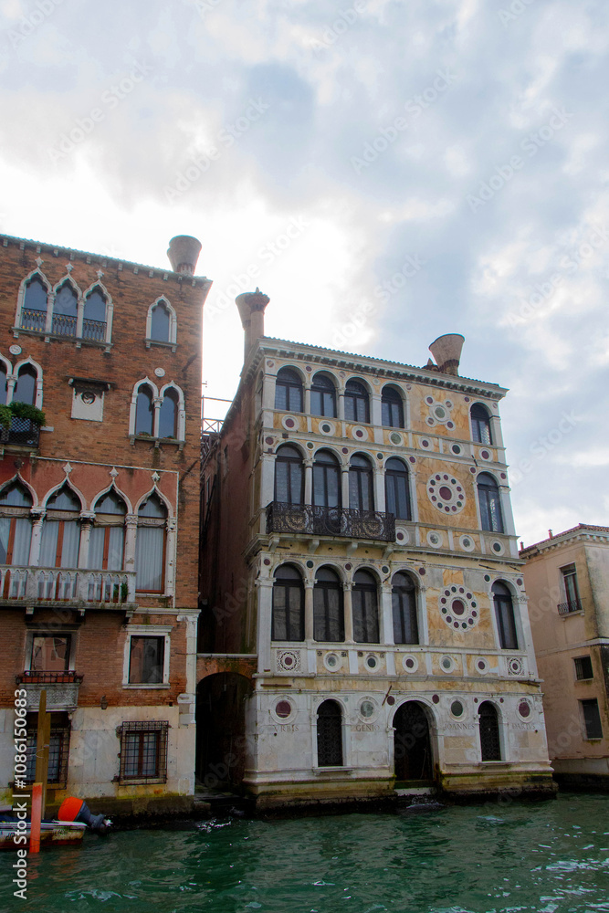A view of historic Venetian buildings along the Grand Canal, showcasing classic Italian architecture. The iconic canal waters reflect the facades, with boats and gondolas adding to the charm of Venice