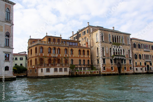 A view of historic Venetian buildings along the Grand Canal, showcasing classic Italian architecture. The iconic canal waters reflect the facades, with boats and gondolas adding to the charm of Venice