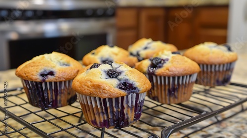 A fresh batch of blueberry muffins cooling on a wire rack in a kitchen.