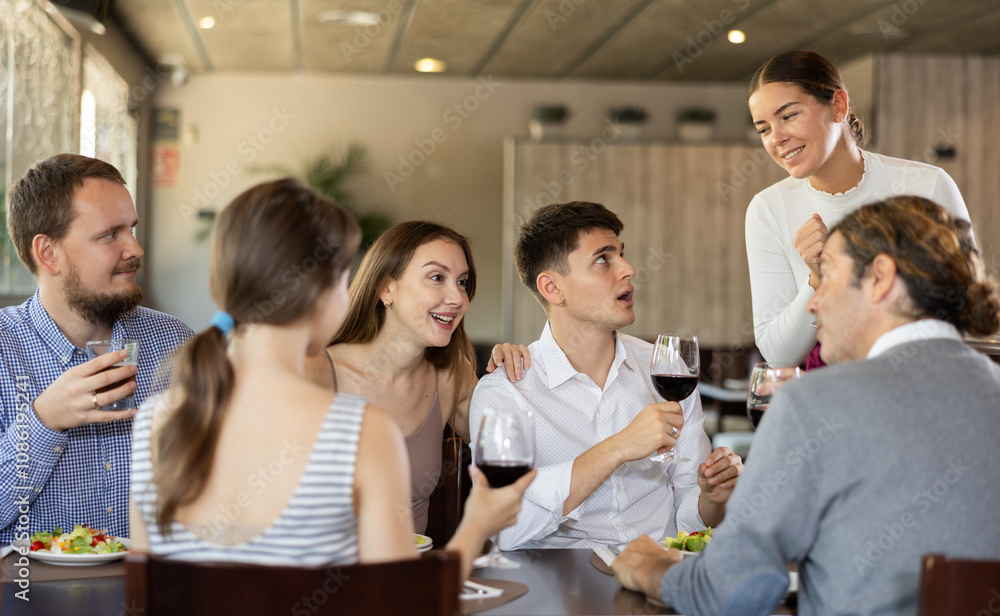 Obraz premium Young female waitress takes order from group of male and female friends in restaurant