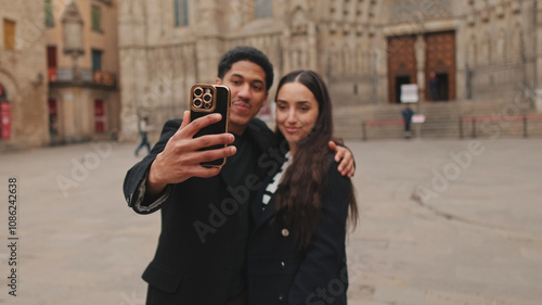 Multiracial couple taking selfie with kiss in front of historic building.