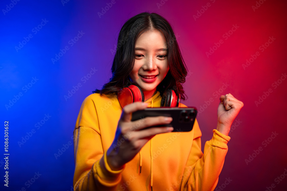 Asian young beautiful woman playing game on smartphone in neon background. Asian young beautiful woman playing game on smartphone in neon background.