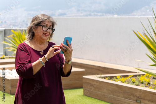 Wallpaper Mural Senior Latina woman looking at her cell phone smiling in the garden Torontodigital.ca