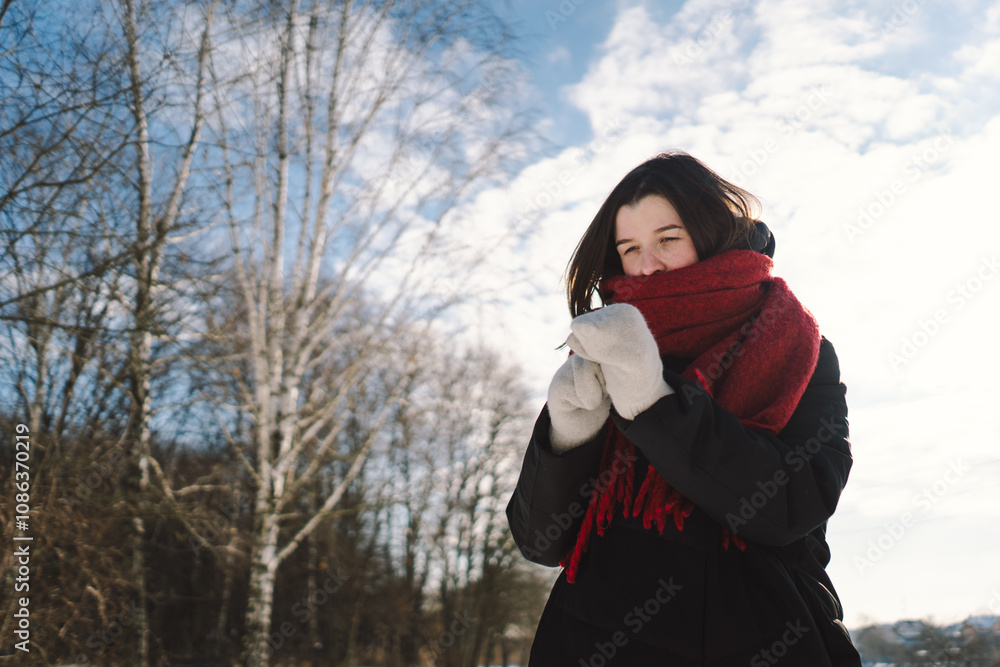 A smiling woman with a red scarf enjoys a snowy winter day in a serene forest setting beneath a bright blue sky. Christmas and New Year celebration concept. A smiling woman with a red scarf enjoys a snowy winter day in a serene forest setting beneath a bright blue sky. Christmas and New Year celebration concept.