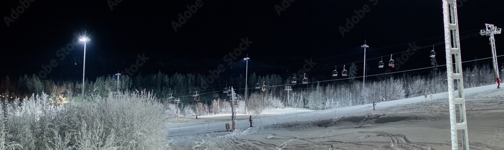 Banner with funicular moving at night in winter in spotlight. Ground and forest covered with snow in the distance. Ski slope, Doing winter sports. Extreme and countryside resort. Banner with funicular moving at night in winter in spotlight. Ground and forest covered with snow in the distance. Ski slope, Doing winter sports. Extreme and countryside resort.