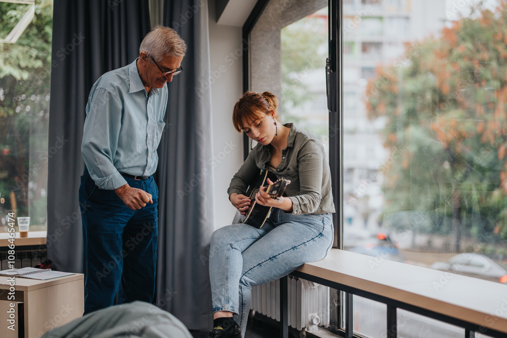 Obraz premium Senior professor guides a young student playing guitar in a contemporary classroom. The scene depicts a supportive educational environment with natural lighting and engaged learning.