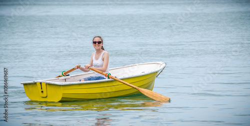 Fotografía Young woman rowing a small yellow boat on calm water
