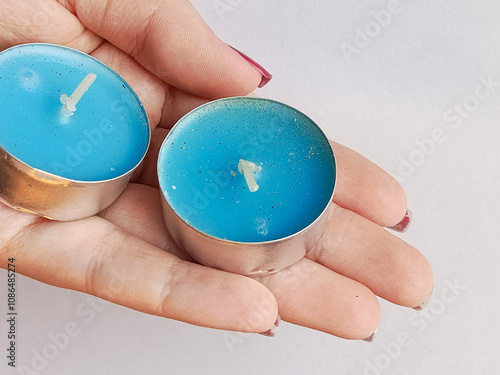 A woman's hand holds blue scented candles on a white background. A candle in a metal cup. The background for the advertisement, the place for the text. photo