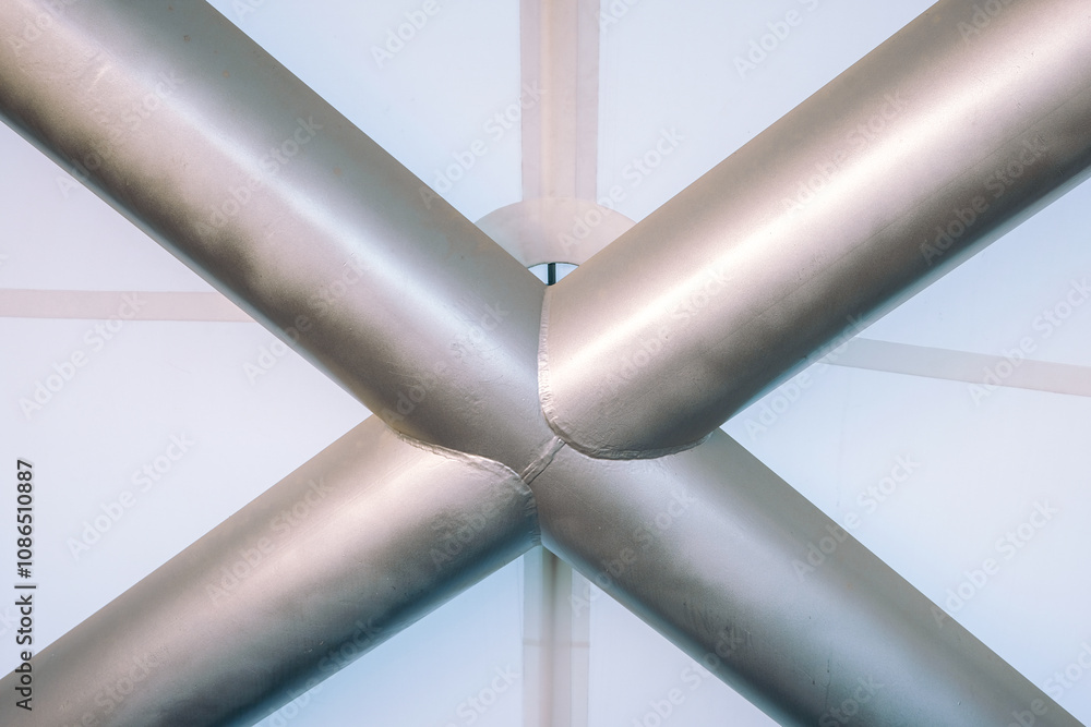 Naklejka premium Metallic intersecting pipes creating a geometric pattern in an industrial setting