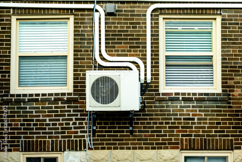 mini split air conditioner / heat pump exterior unit monuted on the brick wall of an older apartment building between two windows shot toronto beaches neighbourhood photo