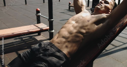 Athletic man doing sit up exercise on incline bench at gym outdoors. Sporty male has workout, training abs muscles and doing crunch with equipment. Fitness Sport Street Workout.