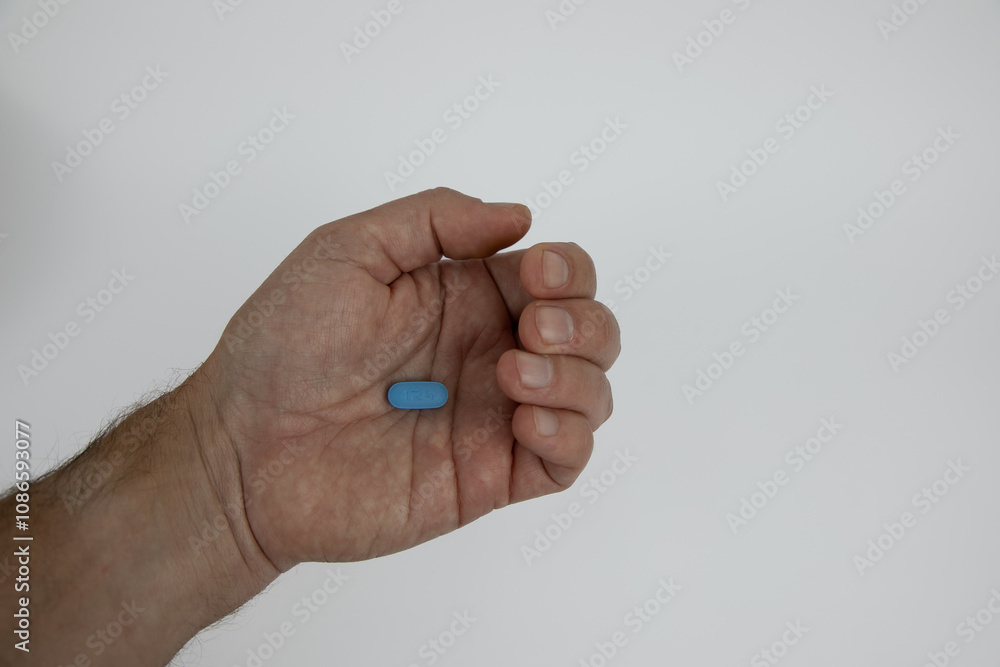 Slightly closed caucasian male hand with a blue pill in the palm of the hand. Hand against white background. Slightly closed caucasian male hand with a blue pill in the palm of the hand. Hand against white background.