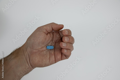 Slightly closed caucasian male hand with a blue pill in the palm of the hand. Hand against white background. 