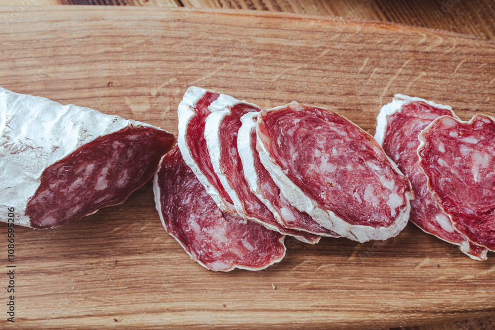 slices of traditional Spanish sausage salami fuet or dry sausage, covered with fermented mold on a wooden table. slices of traditional Spanish sausage salami fuet or dry sausage, covered with fermented mold on a wooden table.