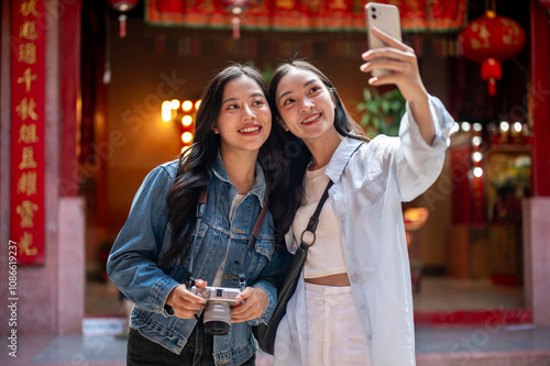 Two happy Asian female friends taking a selfie together while visiting a stunning Chinese shrine. photo