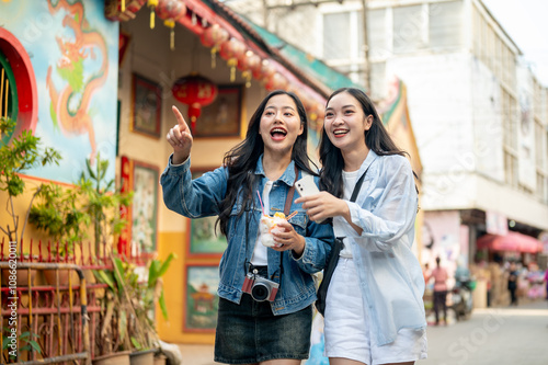Obraz na płótnie Two joyful young Asian female tourists explore the city in Thailand together, fi