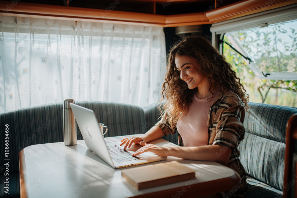 Young beautiful woman is camping in nature, sitting in her caravan and working on a notebook. Caravan as homeoffice, working remotely. Young beautiful woman is camping in nature, sitting in her caravan and working on a notebook. Caravan as homeoffice, working remotely.
