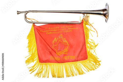 The image shows a blowgun with a red banner attached to it. The banner is decorated with yellow fringe and embroidery containing symbols and text, presumably related to the pioneer movement or ceremon photo