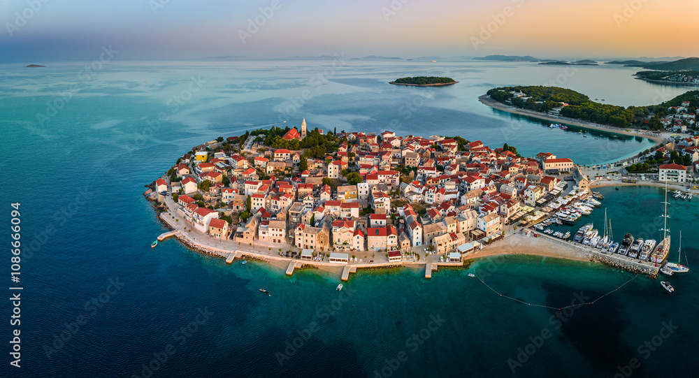 Primosten, Croatia - Aerial panoramic view of Primosten peninsula, St. George's Church and old town on a sunny summer morning in Dalmatia, Croatia. Golden sky, yacht marina and turquoise sea water