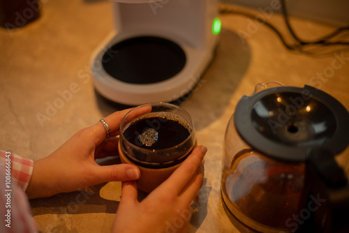 A young woman prepares coffee and tea in the kitchen, enjoying a peaceful moment. Perfect for themes of home life, kitchen activities, and relaxation photo