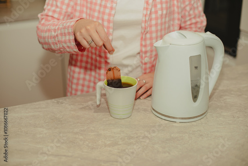 A young woman prepares coffee and tea in the kitchen, enjoying a peaceful moment. Perfect for themes of home life, kitchen activities, and relaxation photo