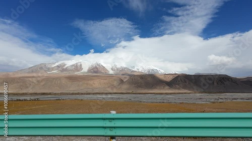 Driving on asphalt road passing through valley in snow mountains on sunny autumn day in Xinjiang, China, POV side view from the car, 4k real time footage, travel concept. photo