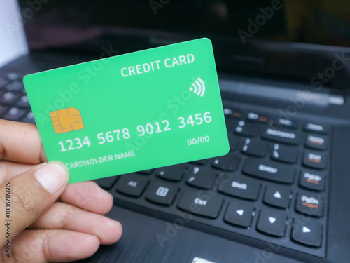 hand holding a credit card with a visible chip and contactless symbol, shown over a laptop keyboard, symbolizing online payment or financial transactions photo