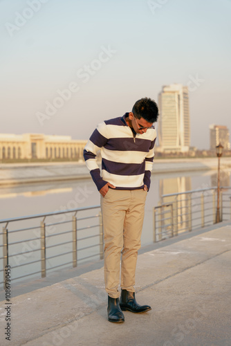 A man in a striped shirt stands on a bridge overlooking a body of water