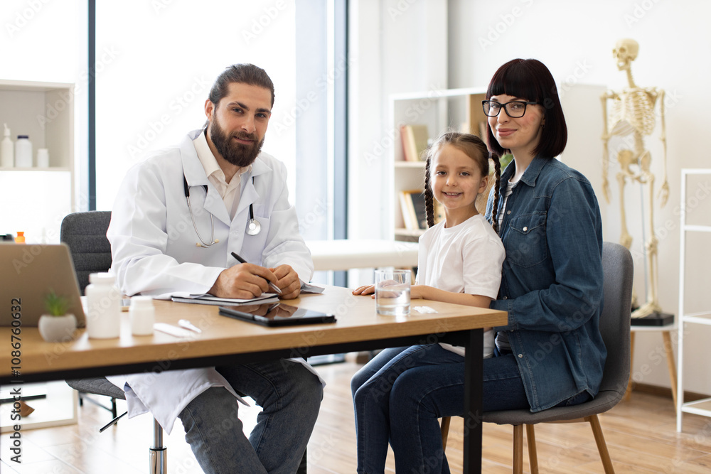 Male doctor interacting with young girl and mother in medical office. Image features Caucasian adult male doctor, Caucasian young girl with braids, and Caucasian adult female mother. Male doctor interacting with young girl and mother in medical office. Image features Caucasian adult male doctor, Caucasian young girl with braids, and Caucasian adult female mother.