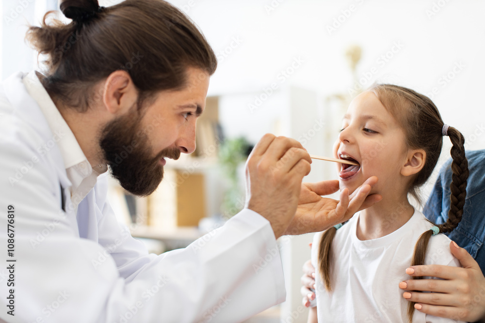 © sofiko14 - Caucasian male doctor examines young Caucasian girl's throat using a wooden tongue depressor. Girl sits calmly in medical office setting, showing a trustful patient-doctor interaction.