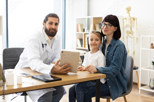 Obraz na plátně Caucasian male doctor consults mother and little girl about test results in modern clinic