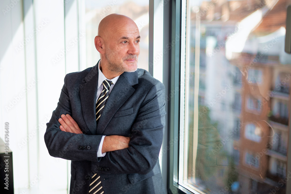 Fototapeta premium Mature businessman standing in a modern office and looking out of the window