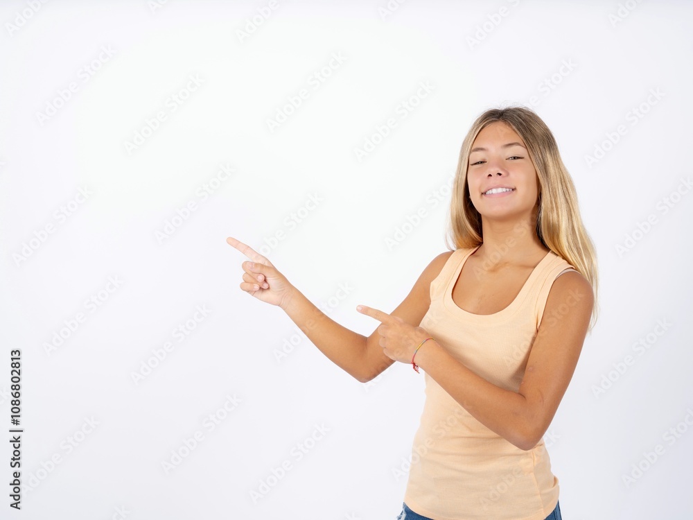 Beautiful teen girl wearing sleeveless t-shirt indicating finger empty space showing best low prices, looking at the camera Beautiful teen girl wearing sleeveless t-shirt indicating finger empty space showing best low prices, looking at the camera