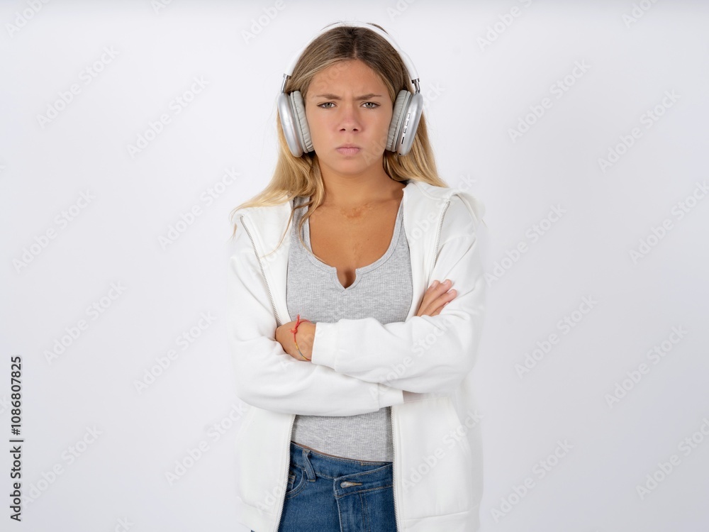 Gloomy dissatisfied Beautiful teen girl wearing white jacket looks with miserable expression at camera from under forehead, makes unhappy grimace