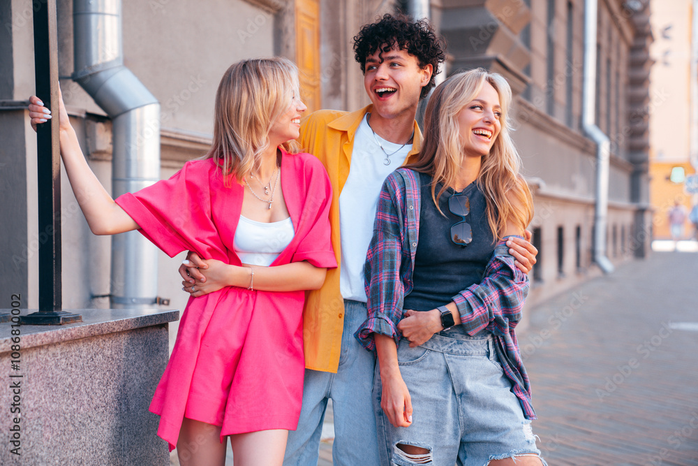 Group of young three stylish friends posing in the street. Fashion man and two cute female dressed in casual summer clothes. Smiling models having fun. Cheerful women and guy outdoors