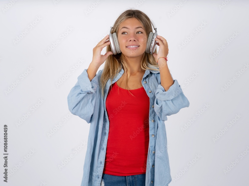 Beautiful teen girl wearing denim jacket wears stereo headphones listens music concentrated aside. People hobby lifestyle concept Beautiful teen girl wearing denim jacket wears stereo headphones listens music concentrated aside. People hobby lifestyle concept