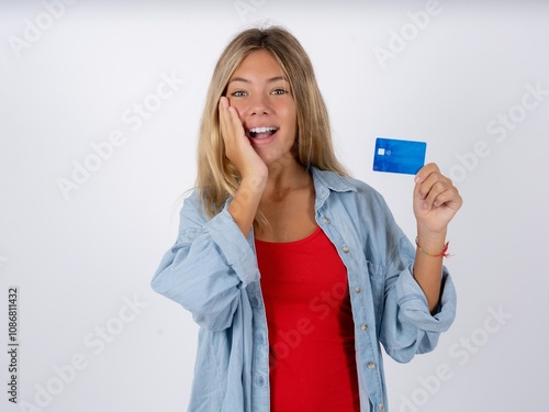 Astonished positive Beautiful teen girl wearing denim jacket arm face hold bank plastic card impressed functions photo